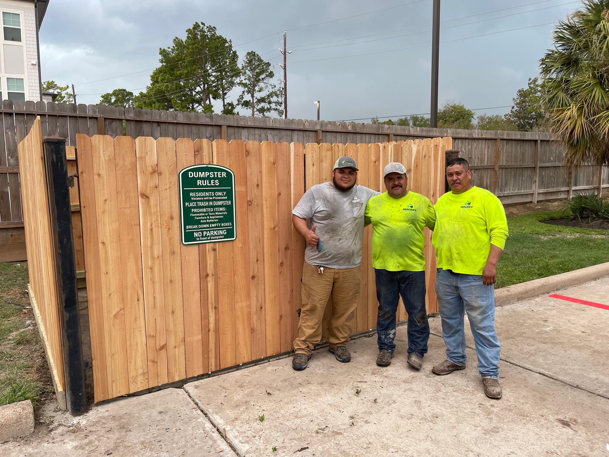 Mackey crew beside a wooden dumpster enclosure